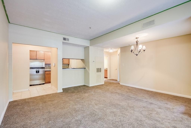 unfurnished living room featuring baseboards, visible vents, a notable chandelier, and light colored carpet