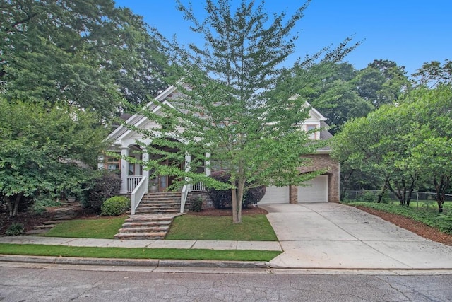 view of property hidden behind natural elements featuring a front lawn, covered porch, and a garage