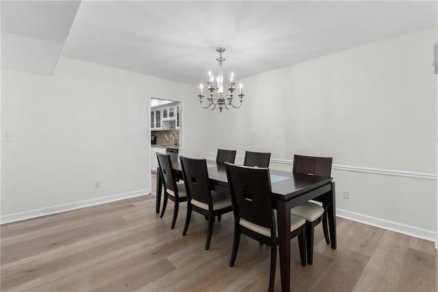 dining space featuring light wood-style flooring, baseboards, and a chandelier