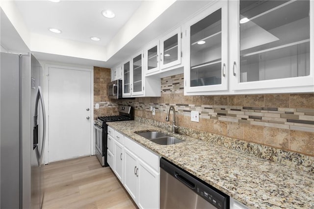 kitchen with decorative backsplash, light wood-style flooring, appliances with stainless steel finishes, white cabinetry, and a sink