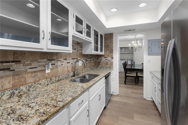 kitchen with stainless steel appliances, decorative backsplash, white cabinets, a sink, and light wood-type flooring