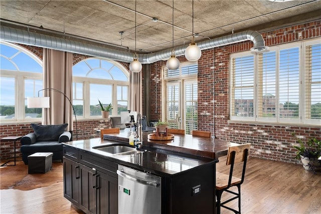 kitchen featuring dishwasher, a kitchen island with sink, pendant lighting, brick wall, and light hardwood / wood-style floors