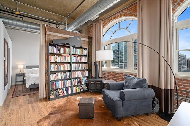 living area featuring hardwood / wood-style flooring, brick wall, a healthy amount of sunlight, and a wood stove