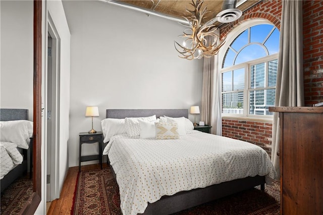 bedroom featuring hardwood / wood-style flooring, a chandelier, and brick wall