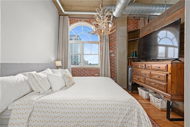 bedroom featuring brick wall, hardwood / wood-style floors, and a notable chandelier