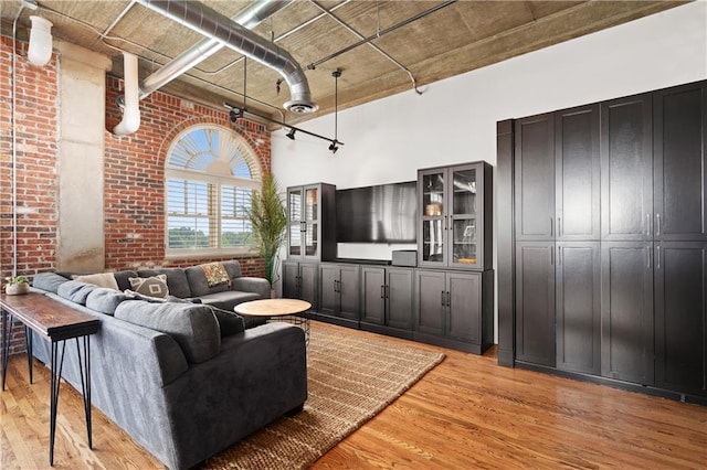 living room with a towering ceiling, brick wall, and light wood-type flooring