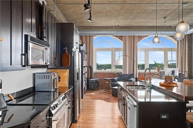 kitchen featuring sink, a wood stove, a kitchen island with sink, light hardwood / wood-style floors, and stainless steel appliances