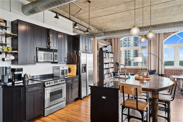 kitchen featuring stainless steel appliances, sink, pendant lighting, brick wall, and light hardwood / wood-style floors