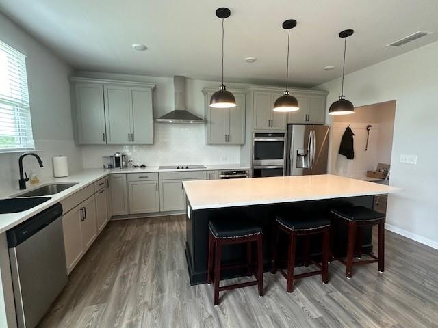 kitchen with decorative backsplash, appliances with stainless steel finishes, light hardwood / wood-style flooring, sink, and wall chimney range hood