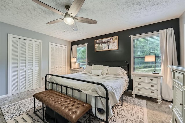 carpeted bedroom with baseboards, multiple windows, two closets, and a textured ceiling