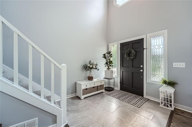 foyer featuring baseboards, visible vents, stairs, and a towering ceiling