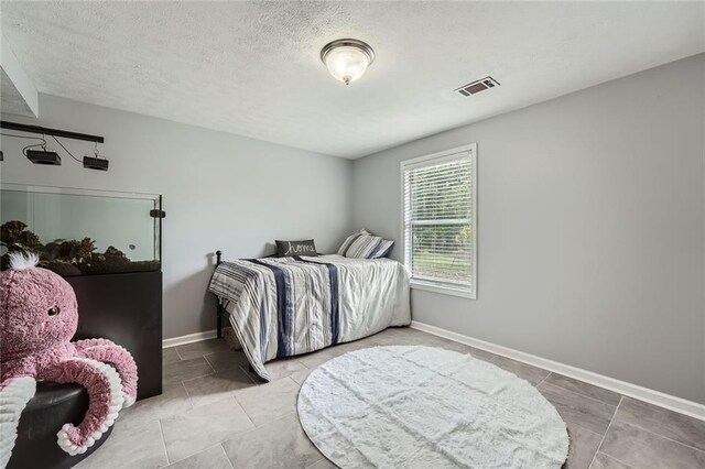 tiled bedroom with baseboards, a textured ceiling, and visible vents