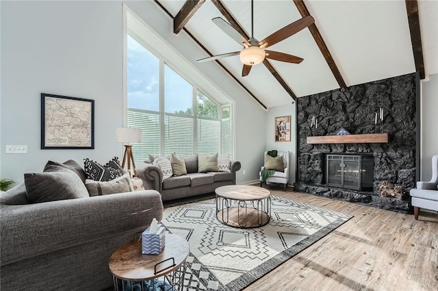 living area featuring a ceiling fan, a stone fireplace, wood finished floors, high vaulted ceiling, and beamed ceiling