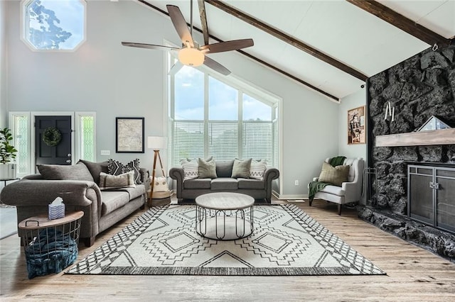 living area featuring ceiling fan, a fireplace, high vaulted ceiling, wood finished floors, and beamed ceiling