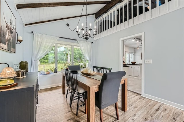 dining space with baseboards, lofted ceiling with beams, light wood finished floors, and a chandelier