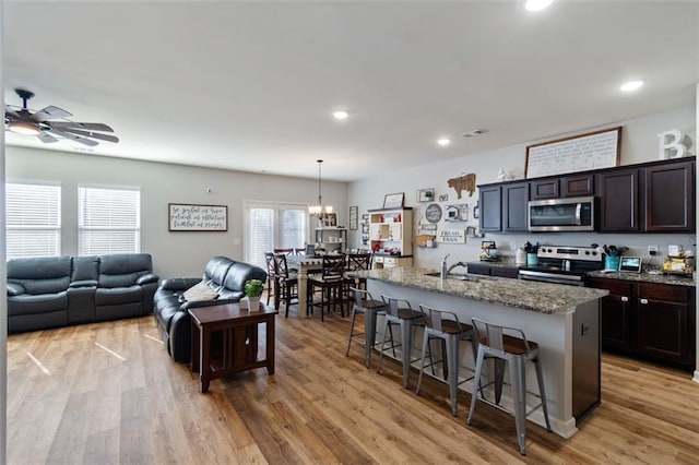 kitchen with a center island with sink, light stone counters, a breakfast bar, and appliances with stainless steel finishes