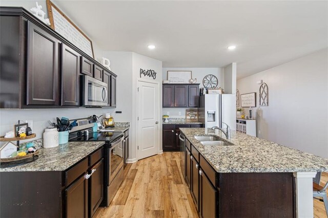 kitchen featuring stainless steel appliances, sink, a kitchen island with sink, light hardwood / wood-style flooring, and dark brown cabinets