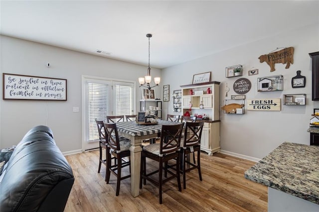 dining space with visible vents, light wood-style flooring, baseboards, and an inviting chandelier