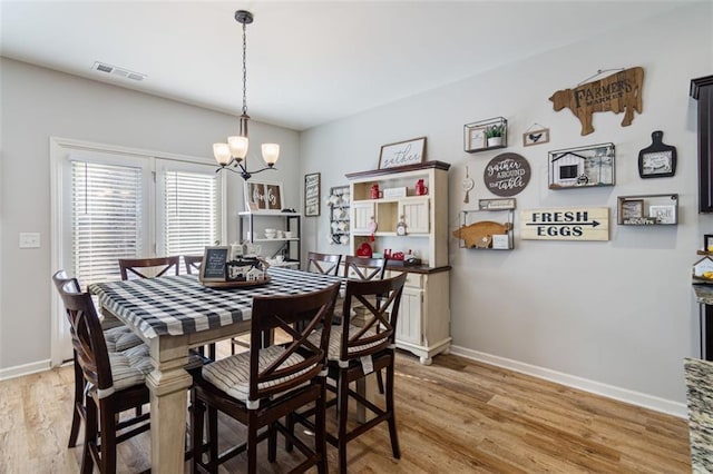 dining area with a chandelier, light wood-type flooring, visible vents, and baseboards