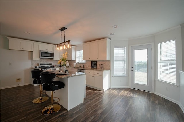 kitchen with appliances with stainless steel finishes, white cabinetry, light stone countertops, a kitchen island, and decorative light fixtures