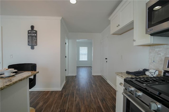 kitchen with appliances with stainless steel finishes, white cabinets, decorative backsplash, ornamental molding, and light stone counters