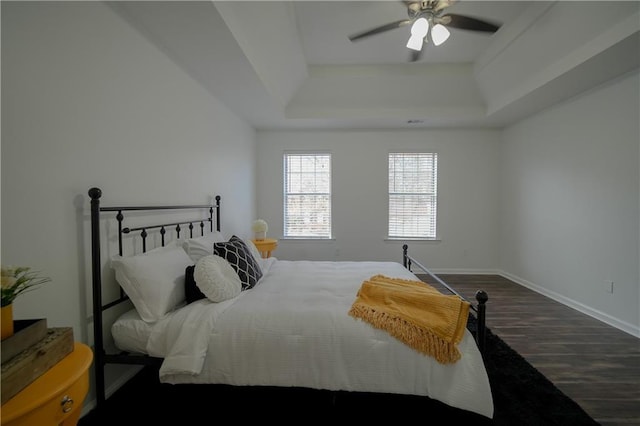 bedroom with dark wood-type flooring, ceiling fan, and a tray ceiling