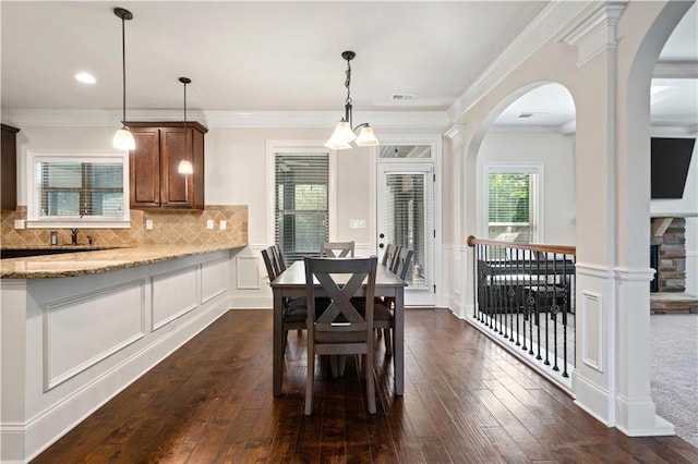 dining space with arched walkways, a decorative wall, dark wood-style floors, and ornamental molding
