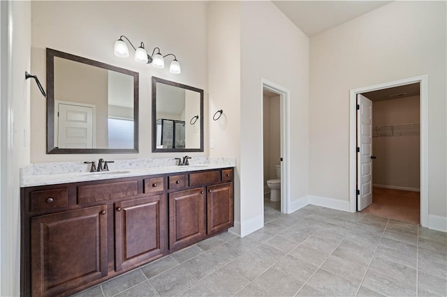 bathroom with a sink, baseboards, toilet, and double vanity