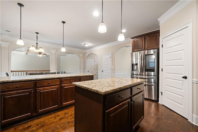 kitchen featuring stainless steel fridge, arched walkways, crown molding, and hanging light fixtures