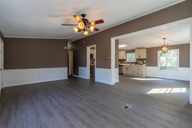 unfurnished living room featuring dark wood-type flooring, ornamental molding, sink, and ceiling fan with notable chandelier