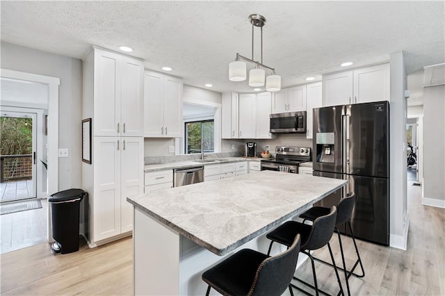 kitchen with hanging light fixtures, a kitchen island, light hardwood / wood-style floors, appliances with stainless steel finishes, and white cabinets