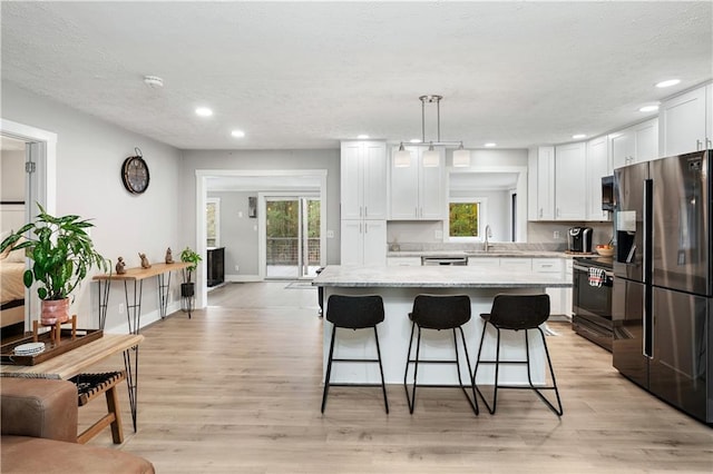 kitchen with light wood-type flooring, stainless steel appliances, pendant lighting, a center island, and white cabinetry