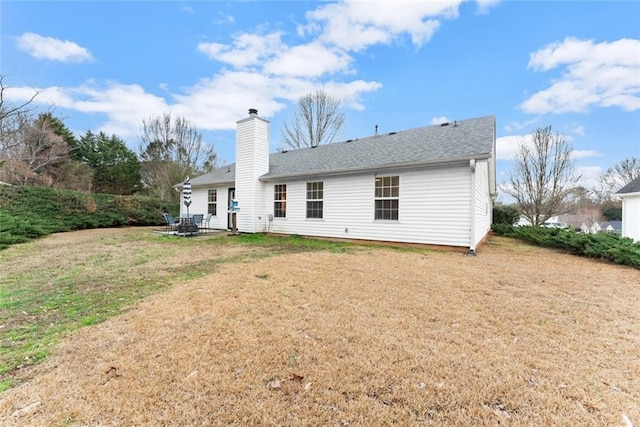 rear view of house featuring roof with shingles, a yard, a chimney, and a patio