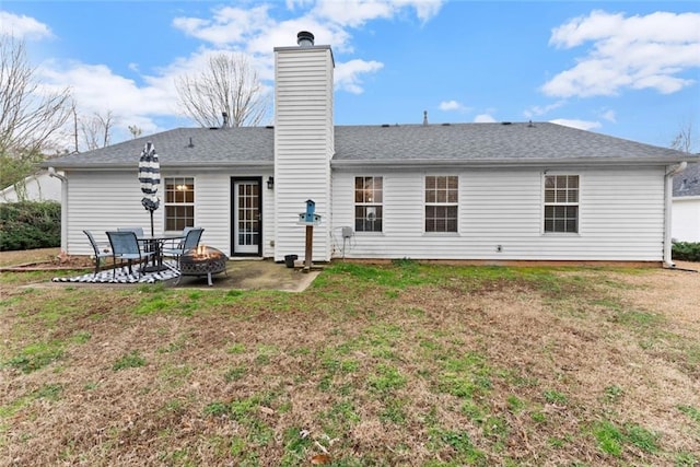 back of property with roof with shingles, a patio, a chimney, a lawn, and an outdoor fire pit