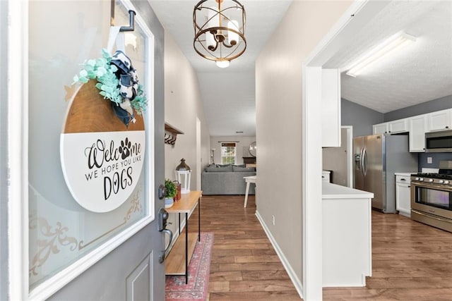 corridor featuring lofted ceiling, light wood-type flooring, baseboards, and a notable chandelier