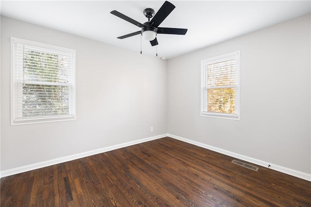 spare room featuring dark wood-type flooring, visible vents, baseboards, and a ceiling fan