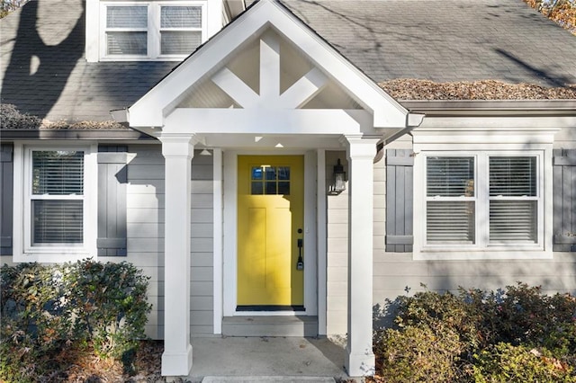 view of exterior entry with roof with shingles