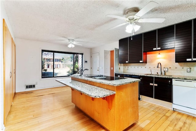 kitchen featuring a kitchen island with sink, a sink, light wood-style floors, decorative backsplash, and dishwasher