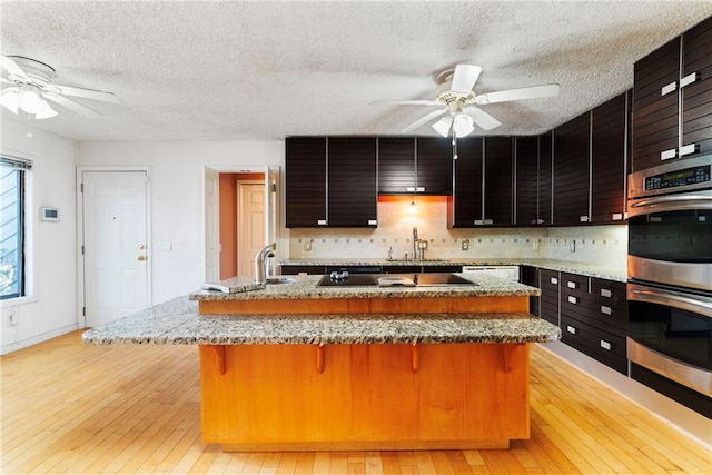 kitchen featuring double oven, black electric stovetop, light wood-style flooring, a breakfast bar, and a sink