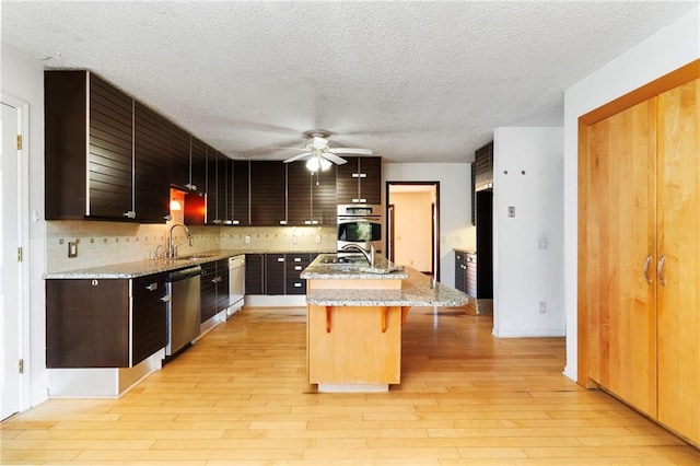 kitchen with light wood-style floors, a kitchen bar, appliances with stainless steel finishes, and a center island with sink