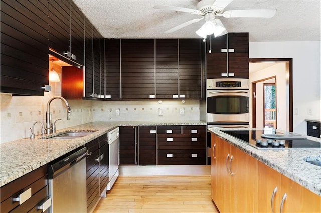 kitchen featuring a textured ceiling, stainless steel appliances, a sink, light wood-style floors, and backsplash