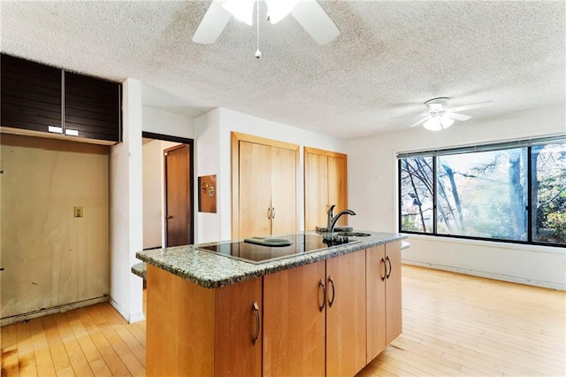 kitchen featuring light wood finished floors, black electric stovetop, a kitchen island with sink, and a ceiling fan