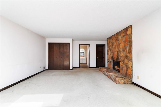 unfurnished living room featuring carpet flooring, a stone fireplace, and baseboards