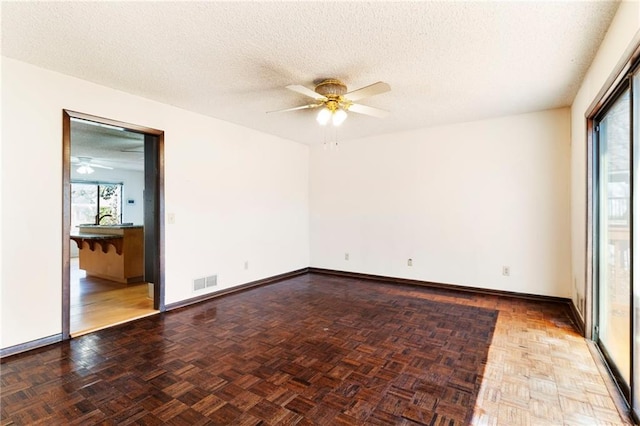 empty room with visible vents, plenty of natural light, a textured ceiling, and ceiling fan