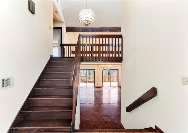 staircase with visible vents, a towering ceiling, and an inviting chandelier