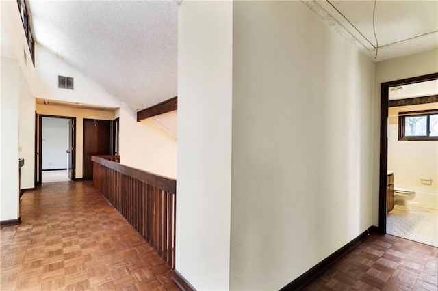 hall featuring lofted ceiling, baseboards, visible vents, and a textured ceiling