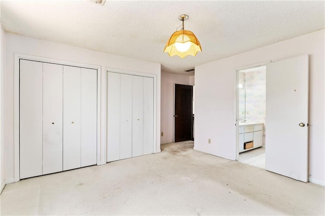 unfurnished bedroom featuring a textured ceiling, ensuite bath, and multiple closets