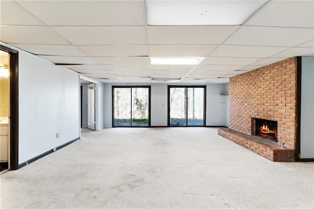 unfurnished living room featuring a drop ceiling, a brick fireplace, carpet flooring, and baseboards