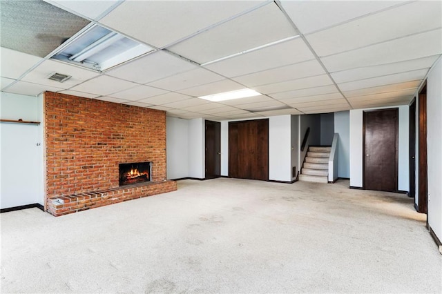 finished basement featuring stairs, a fireplace, a paneled ceiling, and light colored carpet