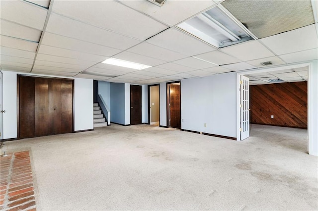 finished basement featuring baseboards, a drop ceiling, stairs, carpet flooring, and wood walls